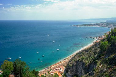 Photograph of the coast of Taormina, on the island of Sicily, during the summer afternoon, houses and trees, boats and the Mediterranean sea and the train statio