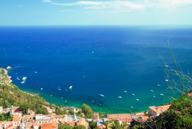 Photograph of the coast of Taormina, on the island of Sicily, during the summer afternoon, houses and trees, boats and the Mediterranean se
