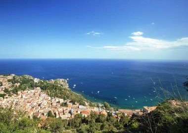 Photograph of the coast of Taormina, on the island of Sicily, during the summer afternoon, houses and trees, boats and the Mediterranean se