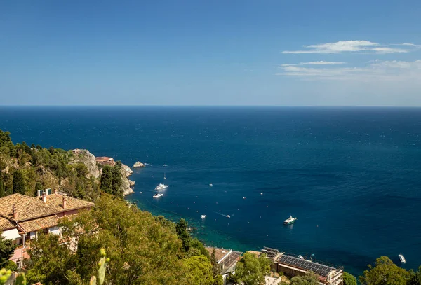 Photograph of the coast of Taormina, on the island of Sicily, during the summer afternoon, houses and trees, boats and the Mediterranean se