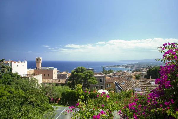 Photograph of the coast of Taormina, on the island of Sicily, during the summer afternoon, houses and trees, boats and the Mediterranean se
