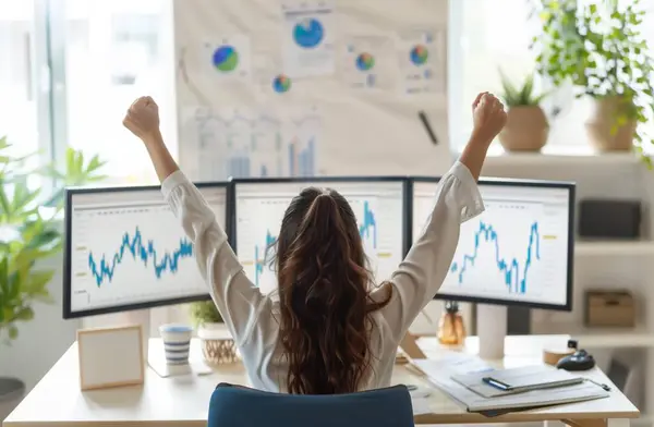 In this empowering image, a woman celebrates a winning trade on the stock market from her desk, her arms raised in victory. With a radiant smile, she exudes confidence and determination, embodying the spirit of success in finance. Behind her, screens