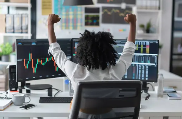In this triumphant image, a black woman celebrates a successful trade on the stock market from her desk, her arms raised in jubilation. With a look of joy and satisfaction, she embodies the spirit of victory and achievement in the world of finance. B