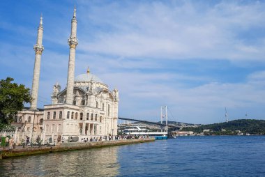 İstanbul 'daki Ortaklık Camii' nin pitoresk bir manzarası, arka planda ikonik Boğaz Köprüsü ve parlak mavi bir gökyüzü..