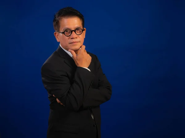 聪明的亚洲中年自信的成功商人穿着蓝色背景的西服站在演播室里 看上去有吸引力和积极的专业领导形象 — 图库照片