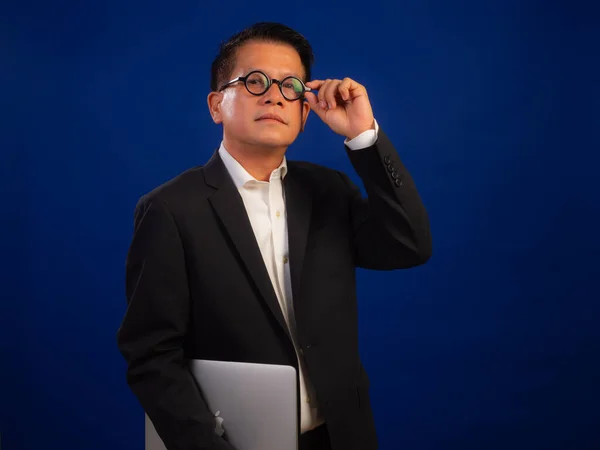 聪明的亚洲中年自信的成功商人身穿西装 手持蓝色背景的笔记本电脑 看上去迷人而积极的专业领导形象 — 图库照片