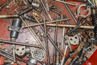 Çeşitli fındıklar, civatalar ve kahverengi plastik bir kapta yağ ile kaplı küçük motor parçaları..
