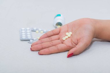 Yatağın üzerinde haplar ve ilaçlarla çevrili genç bir kadının eli. Aşırı doz ve kendi kendini tedavi etmek ölümcül bir uygulamadır. Tema: Depresyon, kendini tedavi.