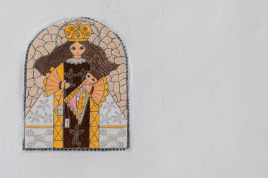 Beyaz bir duvarın solunda Bakire Meryem 'in renkli seramik mozaiği. Metin için alanı olan dini ayrıntı ve temiz, minimalist bir arkaplan.