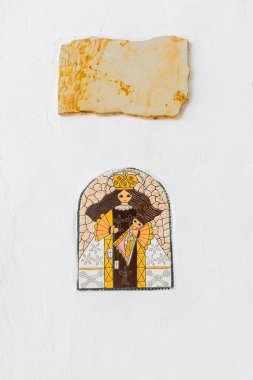 Beyaz bir duvarda üzerinde Barichara taşından bir plaka olan Bakire Meryem mozaiğinin dikey görüntüsü. Geniş negatif alanı olan dini ve kırsal detaylar.