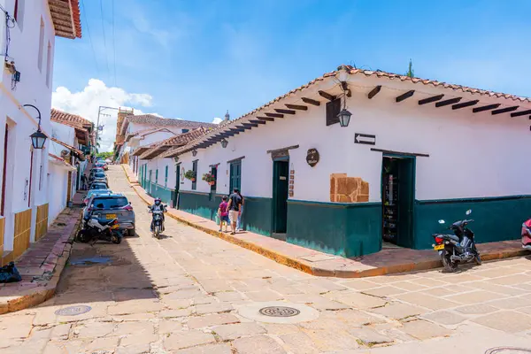 Barichara, Santander, Kolombiya, 11 Ekim 2024. Yeşil üssü olan beyaz bir sömürge evi ana parka giden kaldırım taşı sokağının köşesinde belirgin bir şekilde duruyor. Sahnede park edilmiş arabalar ve motosikletler, tarihi cazibe harmanlanıyor.