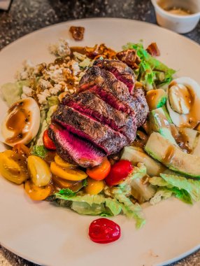 Restoranda beyaz tabakta salatalı biftek.