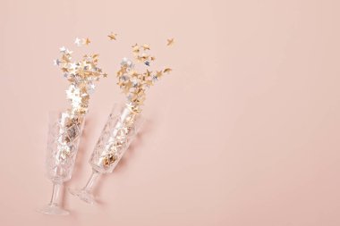 Şampanya ya da pembe arka planda konfetili köpüklü şarap bardakları. Noel, yeni yıl partisi, doğum günü veya düğün kutlaması fikri. Üst görünüm, düz görünüm, kopyalama alanı