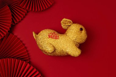 Golden rabbit over red background with paper fans. Text on hare means wishing of fortune, money, prosperity. Lunar new year concept