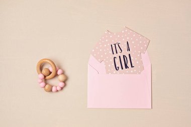 Baby shower, gender reveal party. It's a girl message over paper cut onesie. Flatlay, top view on a beige pastel background. Newborn gifts. Invitation, celebration, greeting card idea