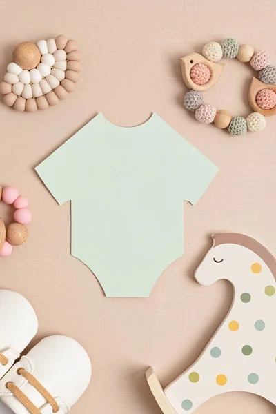 Baby shower, gender reveal party. Empty paper cut onesie. Flatlay, top view on a beige pastel background. Newborn gifts. Invitation, celebration, greeting card idea mockup