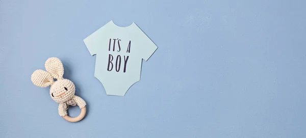 Baby shower, gender reveal party. It's a boy message over paper cut onesie. Flatlay, top view on a blue pastel background. Newborn gifts. Invitation, celebration, greeting card idea