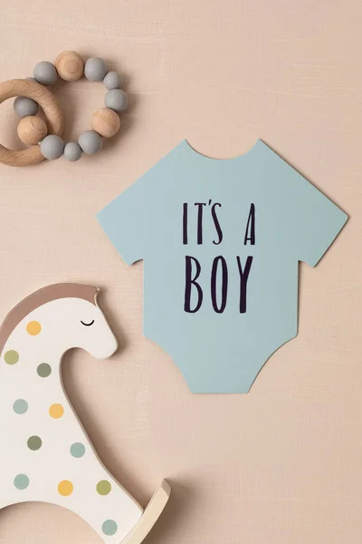 Baby shower, gender reveal party. It\'s a boy message over paper cut onesie. Flatlay, top view on a blue pastel background. Newborn gifts. Invitation, celebration, greeting card idea