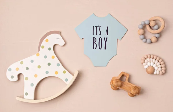 Baby shower, gender reveal party. It\'s a boy message over paper cut onesie. Flatlay, top view on a beige pastel background. Newborn gifts. Invitation, celebration, greeting card idea