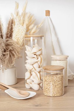 Tahıl çeşitleri, tahıl gevreği ve cam kavanozlarda makarna ve ahşap masada mutfak gereçleri. Sağlıklı dengeli gıda, etik sürdürülebilir yaşam tarzı, sıfır atık, çevre dostu konsept.
