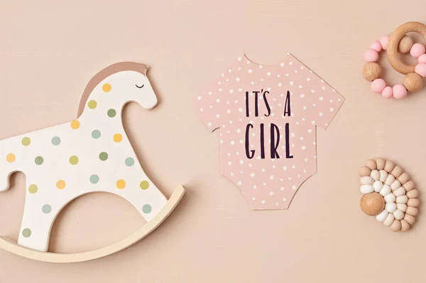 Baby shower, gender reveal party. It\'s a girl message over paper cut onesie. Flatlay, top view on a beige pastel background. Newborn gifts. Invitation, celebration, greeting card idea