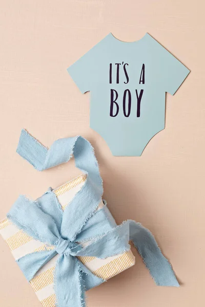 Baby shower, gender reveal party. It's a boy message over paper cut onesie. Flatlay, top view. Newborn gifts. Invitation,