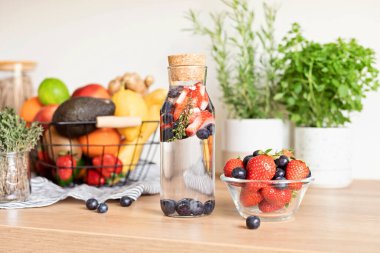 Ahşap masadaki cam şişede çilek ve yaban mersini ile doldurulmuş su. Diyet, detoks, sağlıklı beslenme, kilo verme konsepti
