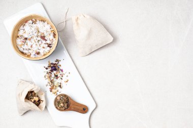 Pamuk torbalarda botanik karışımları, tuz, bitkiler, doğal yağlar. Doğal ilaç, bitkisel ilaç, banyo için karışımlar ve ahşap masa arkasında çay.