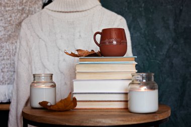 İçinde bir yığın kitap, kupada sıcak içecek ve sıcak battaniye olan kompozisyon. Soğuk hava ve bir fincan kahve için samimi bir okuma sahnesi.