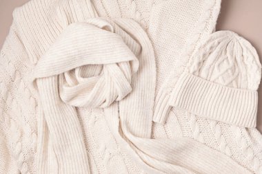 Bej rengi yün süveter, pastel arka planda şapka ve eşarp. Şık bir kadın dış giysisi. Kış aksesuarları