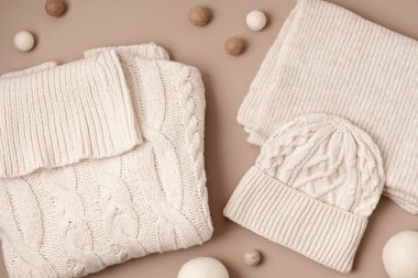 Bej rengi yün süveter, pastel arka planda şapka ve eşarp. Şık bir kadın dış giysisi. Kış aksesuarları