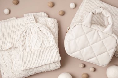 Pastel arka planda bej örülü şişirilmiş çanta ve yün aksesuarlar. Şık bir kadın dış giysisi. Kış aksesuarları