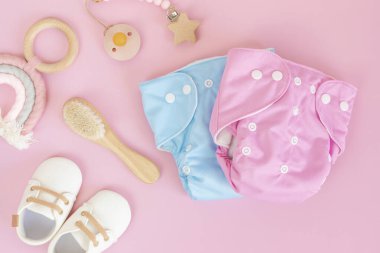 Yeniden kullanılabilir bez bebek bezi, oyuncaklar ve aksesuarlarla yatıyordu. Pembe pastel arka planda çevre dostu bebek bezi. Sürdürülebilir yaşam tarzı, sıfır atık fikri