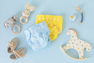 Yeniden kullanılabilir bez bebek bezi, oyuncaklar ve aksesuarlarla yatıyordu. Mavi pastel arka planda çevre dostu bebek bezi. Sürdürülebilir yaşam tarzı, sıfır atık fikri