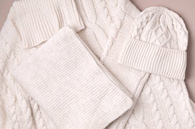 Bej rengi yün süveter, pastel arka planda şapka ve eşarp. Şık bir kadın dış giysisi. Kış aksesuarları