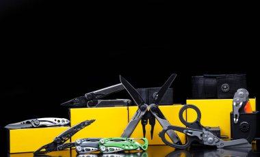 Parlak bir yüzeyde çeşitli çok aletli bıçak ve makas çeşitleri. Kasalar ve kutular onlar için. Koyu arkaplan.