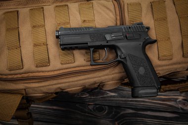 Kahverengi bir sırt çantasında modern siyah bir tabanca. Spor ve nefsi müdafaa için silahlar masanın üzerinde. Kum rengi arkaplan.