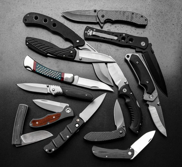 Lots of pocket knives. A variety of folding knives on a gray metallic background.