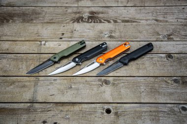Çakıları farklı renklerde katlıyor. Her gün taşımak için cep bıçağı. Avlanmak, spor yapmak ve eğlenmek için çeşitli bıçaklar. Ahşap arkaplan.