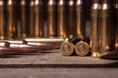 308 kalibrelik tüfek fişeklerine yakın çekim. Ahşap bir yüzeyde silah mühimmatı. Koyu arkaplan.