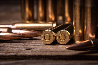 308 kalibrelik tüfek fişeklerine yakın çekim. Ahşap bir yüzeyde silah mühimmatı. Koyu arkaplan.