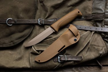 Lastik saplı ve plastik kılıflı modern bıçak. Soğuk çelik antika bir sırt çantasının üzerinde yatıyor. Ahşap arkaplan.