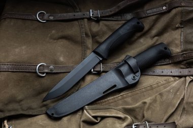 Lastik saplı ve plastik kılıflı modern bıçak. Soğuk çelik antika bir sırt çantasının üzerinde yatıyor. Ahşap arkaplan.