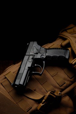 Air gun. Modern pneumatic weapon for air soft, sports and entertainment. A dummy, a copy of a real pistol on a brown military backpack. Dark background. clipart