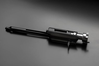 Yarı otomatik bir av tüfeğinin sürgüsü, karanlık bir arkaplanda izole edilmiş, mekanik detaylarını ve parlak tasarımını vurguluyor..