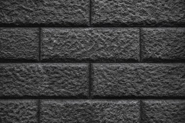 Koyu gri tuğlalardan, pürüzlü ve pürüzlü bir yüzeyi olan dokulu bir duvar. Tuğlalar geleneksel bir şablona göre dizilmiş, düzen ve istikrar hissi yaratıyor..