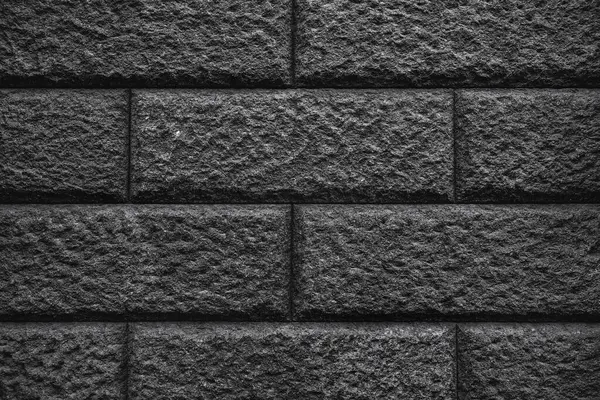 Koyu gri tuğlalardan, pürüzlü ve pürüzlü bir yüzeyi olan dokulu bir duvar. Tuğlalar geleneksel bir şablona göre dizilmiş, düzen ve istikrar hissi yaratıyor..