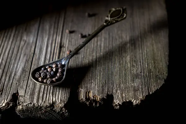 Köy ahşap yüzeyinde siyah karabiberli kaşık, karanlık huysuz atmosfer, mutfak malzemeleri konsepti, baharat fotoğrafçılığı, doğal dokular, eski ahşap arka plan..