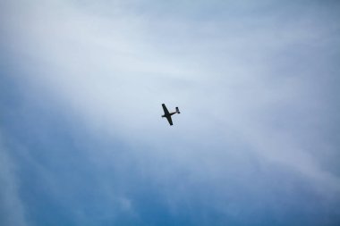 Küçük bir uçak açık mavi bir gökyüzünün arka planına doğru uçuyor ince bulutlu, dingin ve açık bir atmosfer yaratıyor..