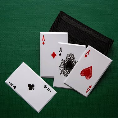 A set of four metal throwing cards, each featuring an Ace from a deck of cards ,Ace of Diamonds, Ace of Spades, Ace of Hearts, Ace of Clubs, is displayed on a green surface with a black pouch. clipart